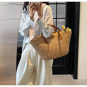 Close-up detail of the woven straw tote bag with brown leather handles and interior pocket