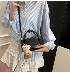Detail of black glossy leather handbag with cute plush bear charm in corduroy overalls
