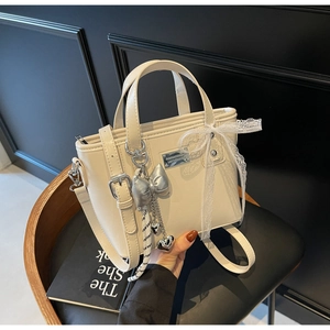 Detail of cream oil-wax leather bucket bag with metallic logo and decorative bow charms