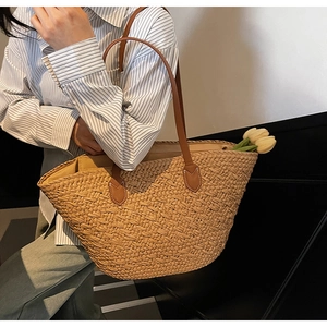 Detailed view of natural straw tote bag featuring brown leather handles and tulip decor