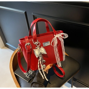 Detail of red oil wax leather bucket bag featuring lace bow and silver heart pendant charm