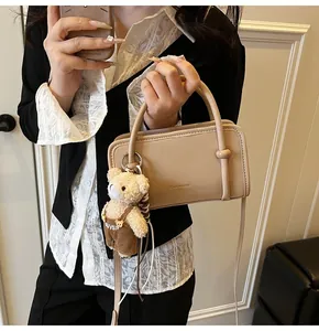 Detail of beige leather handbag featuring unique knotted handle and cute bear charm