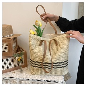 Detail view of woven tote bag with brown leather handles and striped base