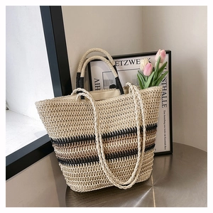 Detail of woven straw tote bag with color-block stripes on a minimalist metal table