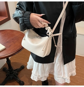 Close-up of beige pleated handbag with drawstring bow details and debossed fashion logo