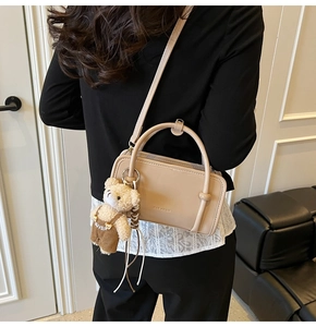 Detail of beige rectangular crossbody bag with plush bear charm and thin shoulder strap