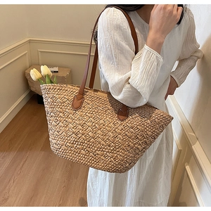 Detail of hand-woven straw tote bag with brown leather shoulder straps and reinforced patches