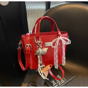 Close-up of a red bucket bag featuring a white lace bow and metallic butterfly charms