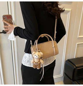 Model wearing cream Boston bag with plush bear charm and adjustable shoulder strap