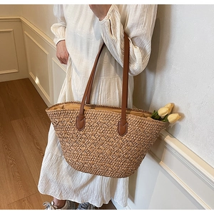 Detailed close-up of woven straw tote bag with brown leather handles and inner fabric lining