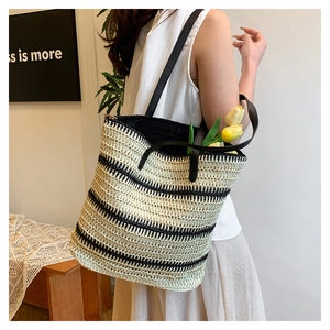 Close-up of a woven straw tote bag with black and white stripes and a black shoulder strap