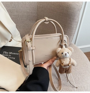 Close-up of cream square handbag with bear charm on a warm minimalist background