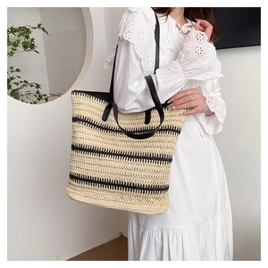 Detail view of woven straw tote bag with black stripes and slender leather shoulder strap