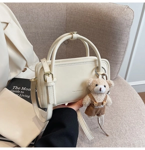 Detail showing cream leather square handbag with adjustable strap and cute teddy bear charm