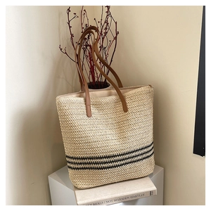 Close-up of woven straw tote bag with black stripes and brown leather shoulder straps