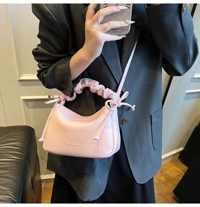 Detail of pink handbag with ruched cloud handle and bow drawstring on grey suit