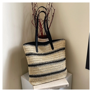 Detail of woven straw tote bag with black stripes and slender straps on display
