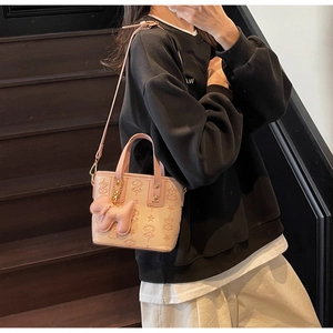 Détail du sac seau rose gaufré avec breloque chien porté par un mannequin chic