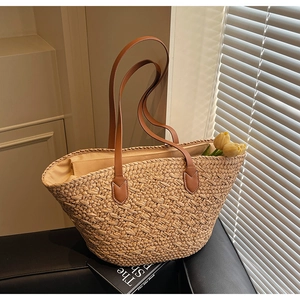 Detailed view of woven straw tote bag with brown leather handles and interior lining