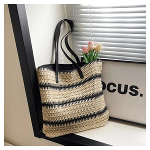 Detail of woven straw tote bag with black stripes and elegant leather shoulder straps