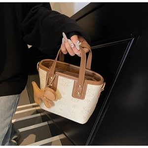 Détail du sac seau crème avec motif étoile, poignées marron et breloque chien