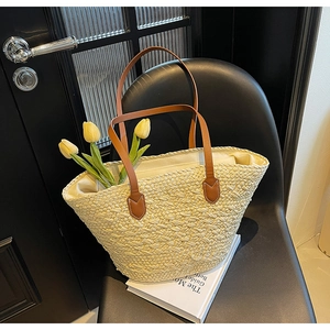 Detail of light beige woven tote bag with brown leather handles and white canvas lining