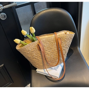 Detail of hand-woven straw tote bag with brown leather handles on a black chair