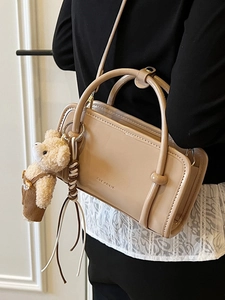 Minimalist beige rectangular handbag with bear charm and tassel shown on a model
