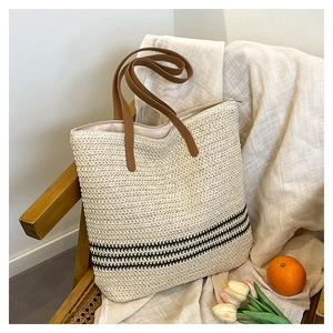 Detailed weave pattern of cream straw tote bag with brown leather handles and black stripes