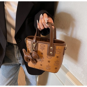 Détail du sac seau en cuir PU gaufré caramel avec breloque chien porté par un modèle