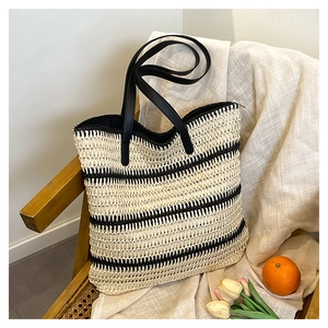 Detail of woven straw tote bag with black stripes on a wooden chair with flowers