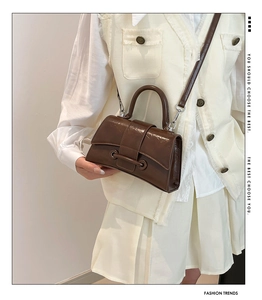 Detail of a dark brown glossy crossbody square bag with vintage texture and silver hardware