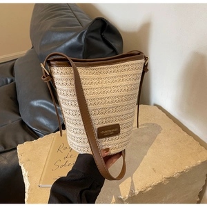 Detail of woven straw bucket bag with dark brown leather trim on stone pedestal