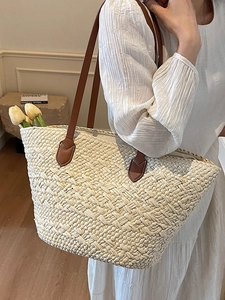 Minimalist beige woven straw tote bag with brown leather handles for a beach holiday