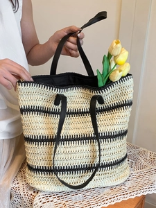Large woven tote bag with black and white stripes and leather handles in a summer setting