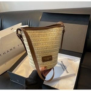 Detail of woven straw bucket bag with dark brown leather trim inside a black gift box