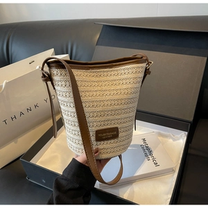 Detailed view of woven straw bucket bag with brown leather trim and shoulder strap