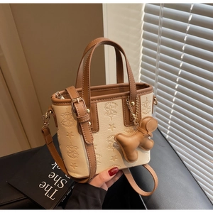 Détail du sac seau beige gaufré avec bordure marron et pendentif de chien en cuir