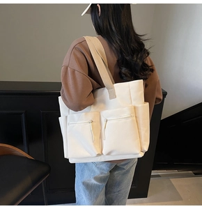 Detail of off-white canvas tote bag featuring double front zipper pockets and side pockets
