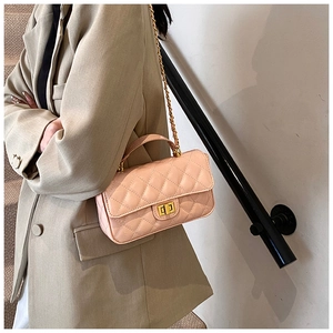 Pink quilted crossbody bag with gold chain strap shown on a model in a beige suit