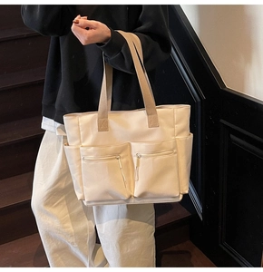 Detail of off-white canvas tote bag featuring dual front zipper pockets and side pockets