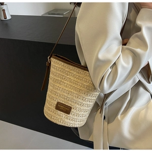 Close-up of woven straw bucket bag with dark brown leather trim and brand label detail