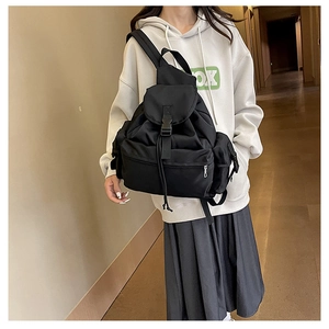 Detail of black nylon backpack with flap buckle and drawstring closure worn by model