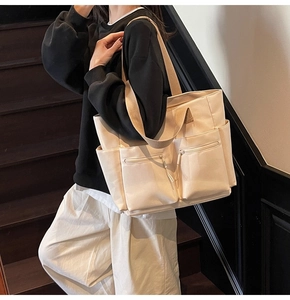 Detail of beige large capacity canvas tote bag featuring front zipper pockets and wide straps