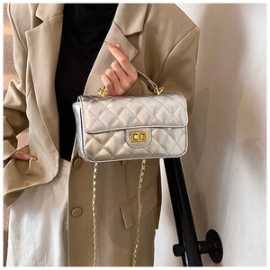 Detail of silver patent leather quilted handbag with gold lock and chain strap on model