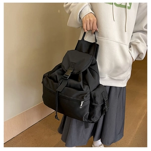Detail of black nylon backpack with buckle closure and drawstring shown by model