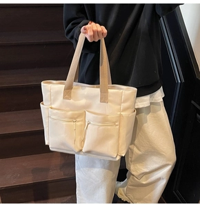 Detail showing two front zipper pockets and side slots on the off-white canvas tote bag