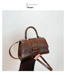 Detail of brown glossy textured leather handbag with unique metal buckle and top handle
