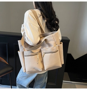 Detail view of a beige canvas tote bag with dual zipper pockets and side compartments