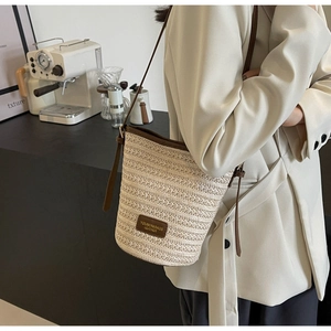 Detail of straw bucket bag with leather trim and adjustable crossbody strap on model